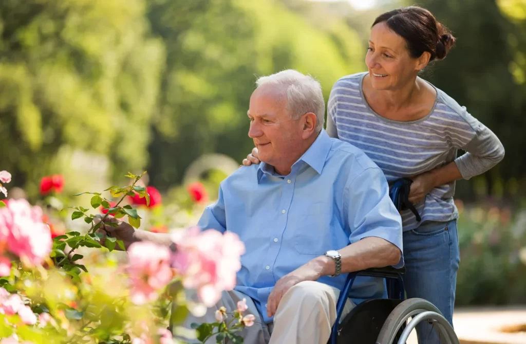 woman pushing senior man in wheelchair through garden pathway